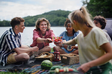 Eine Gruppe multirassischer junger Freunde zeltet in der Nähe eines Sees und grillt gemeinsam, während sie in die Kamera schauen. - HPIF12223