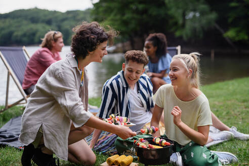 A group of multiracial young friends camping in campsite near lake and and having barbecue together. - HPIF12230