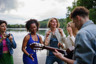 Eine Gruppe junger Freunde hat Spaß am See, lacht und spielt Gitarre. - HPIF12263