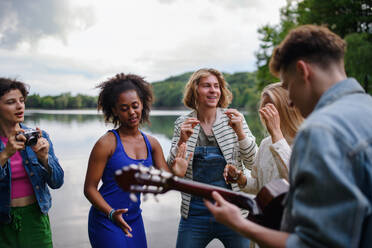 Group of young friends having fun near the lake, laughing and playing guitar. - HPIF12263