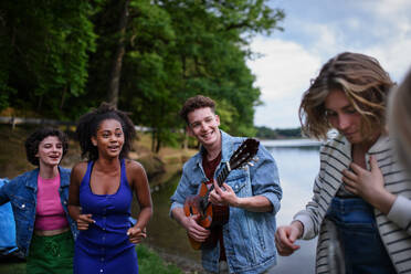 A group of young friends having fun on picnic near a lake, laughing, dancing and playing guitar. - HPIF12264