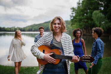 Eine Gruppe junger Freunde hat Spaß am See, lacht und spielt Gitarre. - HPIF12265