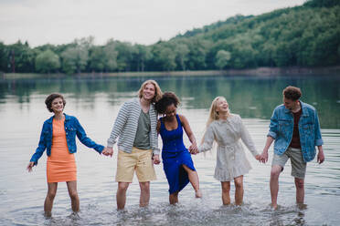 Eine gemischtrassige Gruppe junger Freunde hält sich an den Händen und steht im Sommer im See. - HPIF12284