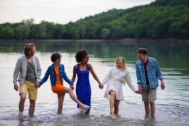 Eine gemischtrassige Gruppe junger Freunde hält sich an den Händen und steht im Sommer im See. - HPIF12285