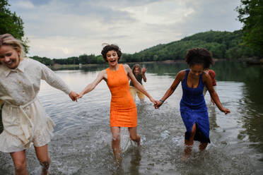 A multiracial group of young friends holding hands,standing in lake in summer and having fun. - HPIF12286