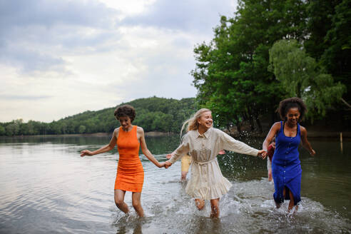 A multiracial group of young friends holding hands,standing in lake in summer and having fun. - HPIF12287