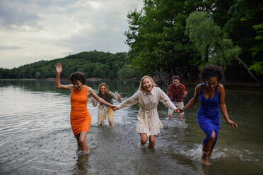 A multiracial group of young friends holding hands,standing in lake in summer and having fun. - HPIF12289