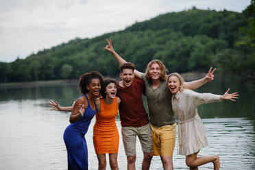 A multiracial group of young friends holding hands and standing in lake in summer. - HPIF12292