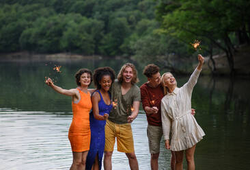 Eine glückliche Gruppe von Freunden zündet Wunderkerzen an und genießt die Freiheit am Strand bei Sonnenuntergang - HPIF12296