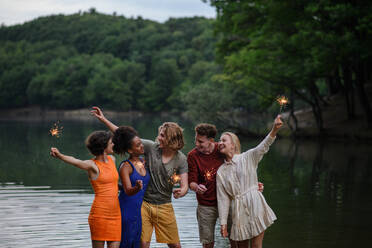 A happy group of friends lighting sparklers and enjoying freedom at beach during sunset - HPIF12297