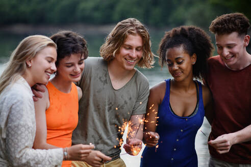 Eine glückliche Gruppe von Freunden zündet Wunderkerzen an und genießt die Freiheit am Strand bei Sonnenuntergang - HPIF12299