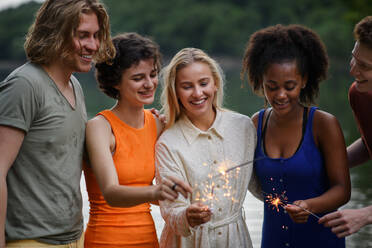 A happy group of friends lighting sparklers and enjoying freedom at beach during sunset - HPIF12301