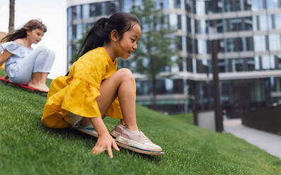 Asian girl trying to skateboarding with her friend in a city park, active kids concept. - HPIF12302