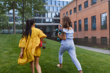 Asiatisches Mädchen bereitet sich mit ihrer Freundin auf das Skateboardfahren in einem Stadtpark vor, aktives Kinderkonzept, Rückansicht. - HPIF12305