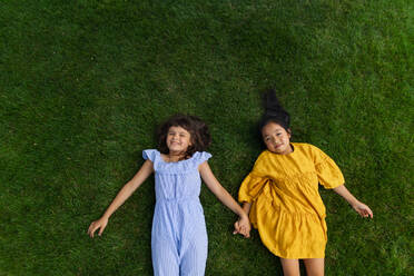Vier glückliche Freunde liegen im Gras, halten sich an den Händen und haben Spaß. Ansicht von oben. - HPIF12308