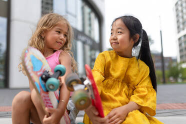 Zwei Mädchen sitzen und halten die Skateboards in der Stadt Straße, aktive Kinder Konzept. niedrigen Winkel Ansicht. - HPIF12337