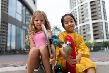 Zwei Mädchen sitzen und halten die Skateboards in der Stadt Straße, aktive Kinder Konzept. niedrigen Winkel Ansicht. - HPIF12338