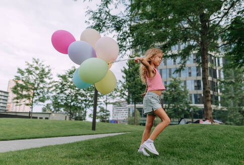 Porträt eines kleinen blonden Mädchens, das mit Luftballons in der Stadt posiert und in die Kamera schaut. - HPIF12342