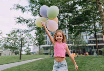 Portrait of little blond girl posing with baloons in city and looking at camera. - HPIF12343