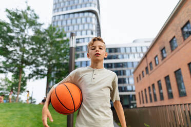 Fröhlicher kaukasischer Junge mit Basketball im öffentlichen Stadtpark, der in die Kamera schaut. - HPIF12345