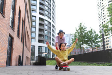 Fröhliches Kind, das auf einem Skateboard sitzt und den Hügel hinunterfährt und in die Kamera schaut. - HPIF12350