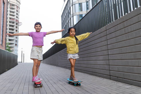 Fröhliches Kind, das auf einem Skateboard sitzt und den Hügel hinunterfährt und in die Kamera schaut. - HPIF12351