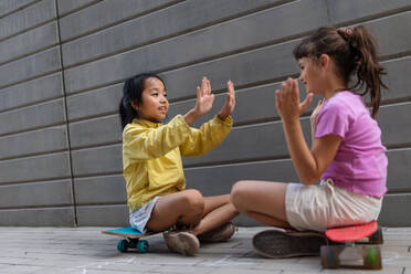Asiatisches Mädchen mit ihrem Freund sitzen in Skateboards in einer Stadt Straße, reden und spielen, aktiven Lebensstil Kinder Konzept. - HPIF12354