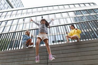 Two girls firends jumping down from concrete wall in city. Low angle view. - HPIF12372