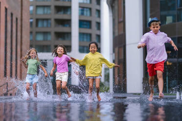 Vier glückliche Kinder spielen und rennen durch einen Stadtbrunnen, während eines Sommertages. - HPIF12375