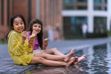 Zwei Mädchen sitzen mit ihren Beinen in einem Brunnen und genießen das Eis und den Sommertag. - HPIF12376