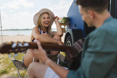 Ein glückliches junges Paar sitzt zusammen vor einem Van, zeltet und spielt auf einer Gitarre. - HPIF12377