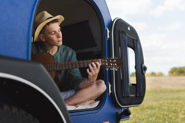 Glücklicher junger Mann, der in einem Van sitzt und auf der Gitarre spielt. - HPIF12379