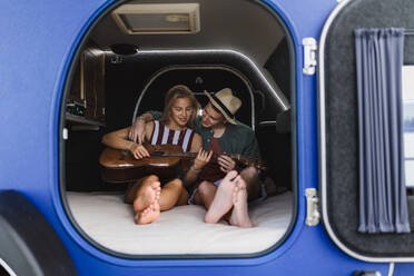 Ein glückliches junges Paar sitzt zusammen in einem Van, zeltet und spielt auf einem Gitarrenstuhl. - HPIF12380