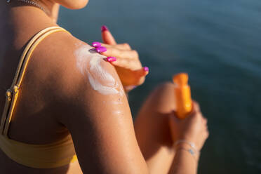 Nahaufnahme einer jungen Frau im gelben Badeanzug, die Sonnencreme auf ihre Haut aufträgt, Konzept für Urlaub und Hautschutz. - HPIF12382