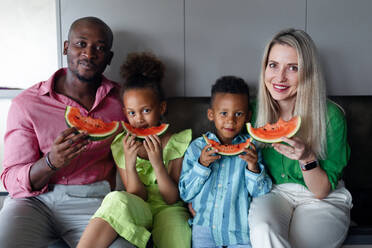 Eine gemischtrassige Familie isst eine Melone in der Küche an einem heißen, sonnigen Tag. - HPIF12392