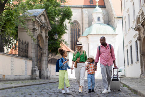 Eine glückliche, gemischtrassige Familie reist mit Koffern durch das alte Stadtzentrum. - HPIF12404