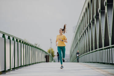 Junge Frau joggt auf einer Stadtbrücke, gesunder Lebensstil und Sportkonzept. - HPIF12437