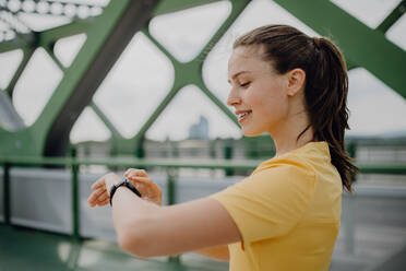 Junge Frau, die in der Stadt eine Smartwatch überprüft und sich auf einen Lauf vorbereitet, Konzept für gesunden Lebensstil und Sport. - HPIF12438