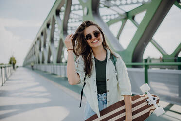 Young woman walking on city bridge with a skateboard. Youth culture and commuting concept. - HPIF12470