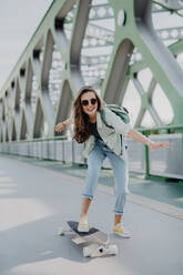 Junge Frau auf einem Skateboard auf einer Brücke in der Stadt, Jugendkultur und Pendeln. - HPIF12472