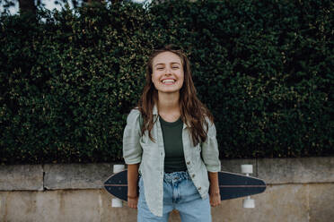 Porträt der jungen glücklichen Frau im Freien mit einem Skateboard. Jugendkultur und Pendeln Konzept. - HPIF12480
