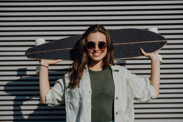 Porträt der jungen glücklichen Frau im Freien mit einem Skateboard. Jugendkultur und Pendeln Konzept. - HPIF12485