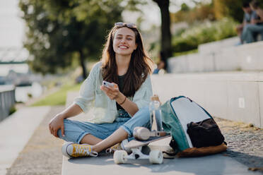 Happy young woman sitting in city park and scrolling smartphone. Youth culture and commuting concept. - HPIF12502