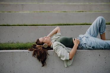 Junge Frau ruht sich im Stadtpark mit geschlossenen Augen aus und genießt die Musik über Kopfhörer. - HPIF12504