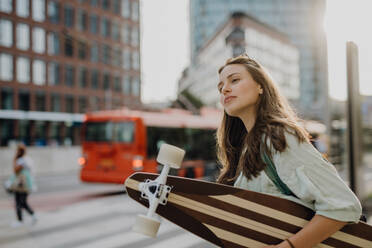 Young woman walking in city with a skateboard. Youth culture and commuting concept. - HPIF12519