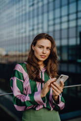 Portrait of beautiful young woman with smartphone outdoor in a city, during sunset. - HPIF12532