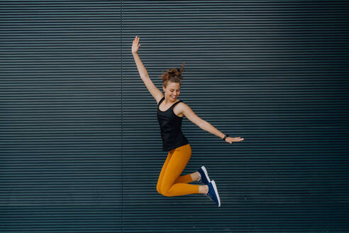Porträt einer jungen aufgeregten Frau, die in einer Stadt im Freien springt. - HPIF12534