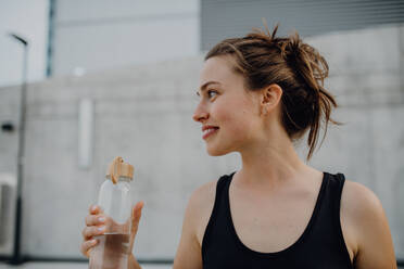 Junge Frau trinkt Wasser beim Joggen in einer Stadt, gesunder Lebensstil und Sportkonzept. - HPIF12549