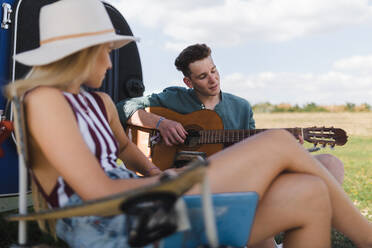 Ein glückliches junges Paar sitzt zusammen vor einem Van, zeltet und spielt auf einer Gitarre. - HPIF12558