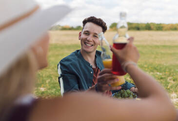 Ein glückliches junges Paar sitzt vor einem Campingwagen und stößt mit Flaschenbier an. - HPIF12563